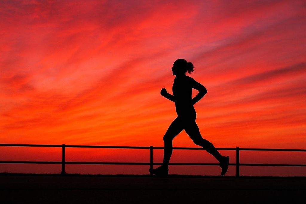 A silhouette of a person running against a vibrant orange and red sunrise or sunset sky. A dark fence runs along the bottom of the image.