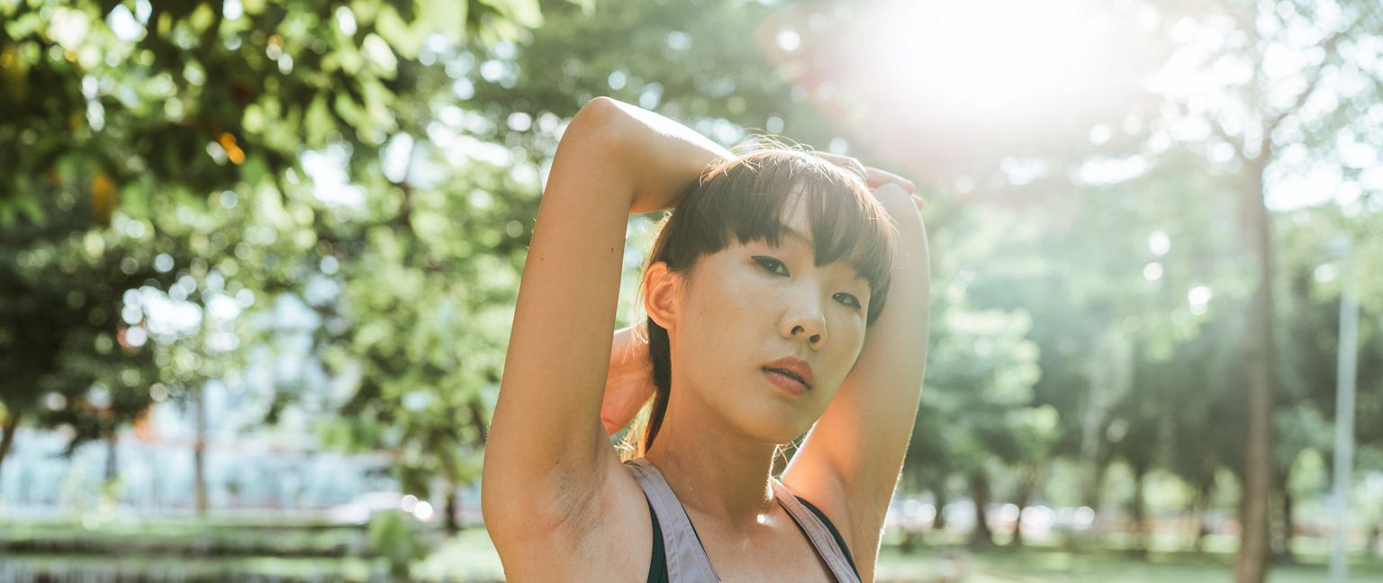 A woman stretches her arm behind her head in a park.