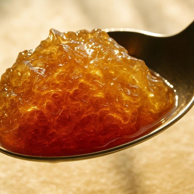 A close-up shot of translucent, golden-brown sea moss gel mounded on a silver spoon, with a soft, warm-toned background.