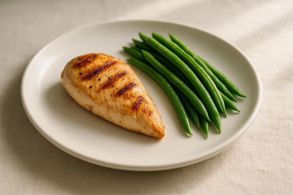 A grilled chicken breast and a pile of green beans on a white plate.