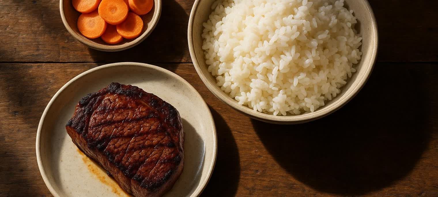 A nutritious meal featuring a perfectly grilled steak on a plate, a bowl of fluffy white rice, and a small bowl of sliced carrots, all arranged on a rustic wooden table.