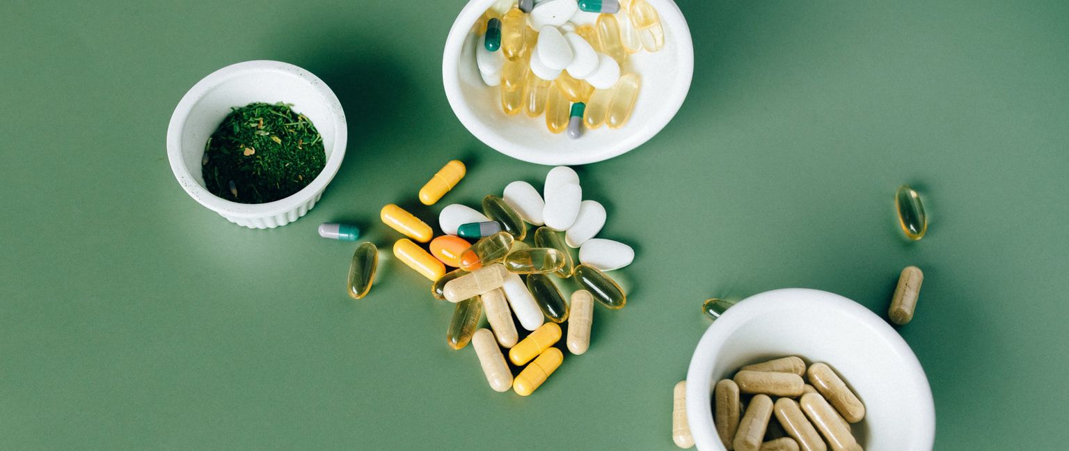 An overhead view of various colorful nutritional supplements in and next to white bowls on a green background.