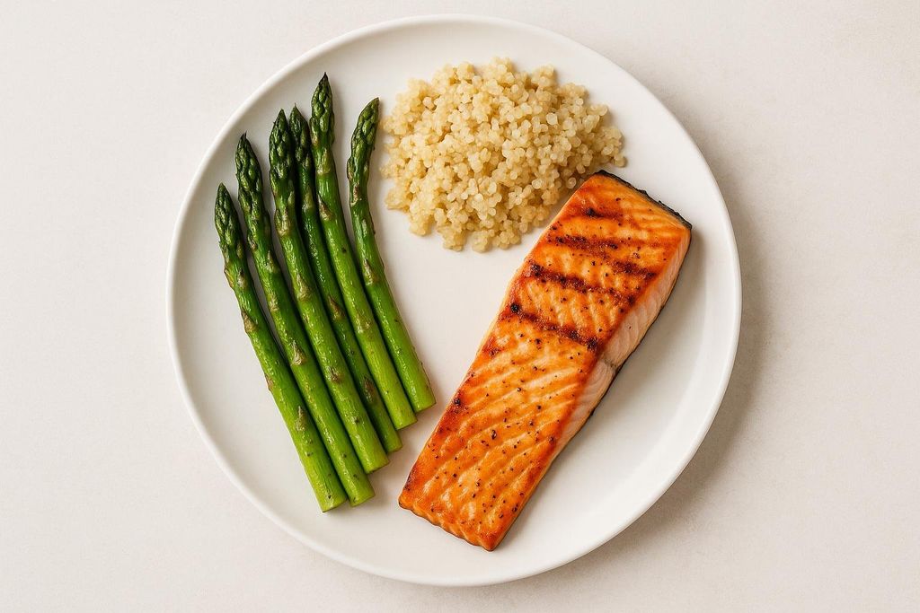 A grilled salmon fillet on a white plate with steamed asparagus and quinoa.