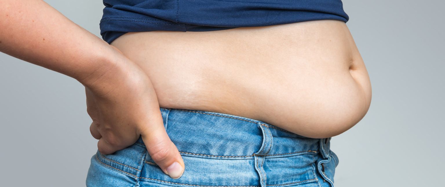 Close up of a woman's belly fat overflowing the top of her jeans.
