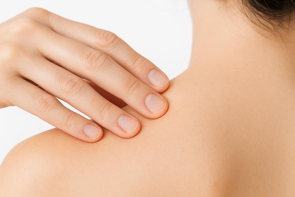 A close-up of a person's hand pressing fingers into their upper shoulder muscle, demonstrating how to find a muscle knot.