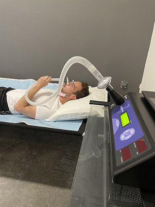A man lies on a bed with a mask attached to tubes, undergoing a Resting Metabolic Rate (RMR) test, possibly related to COVID.