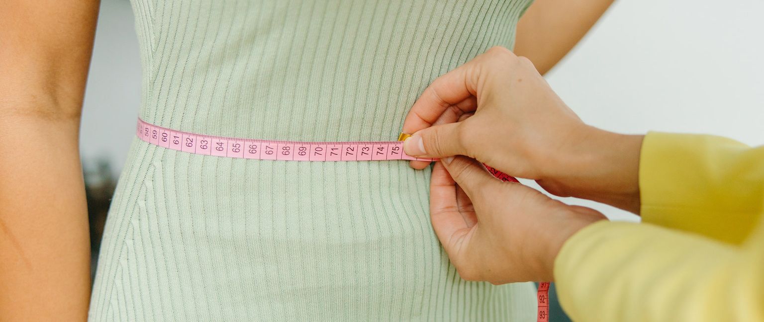 Close up of a nutritionist measuring a person's waist with a pink measuring tape.
