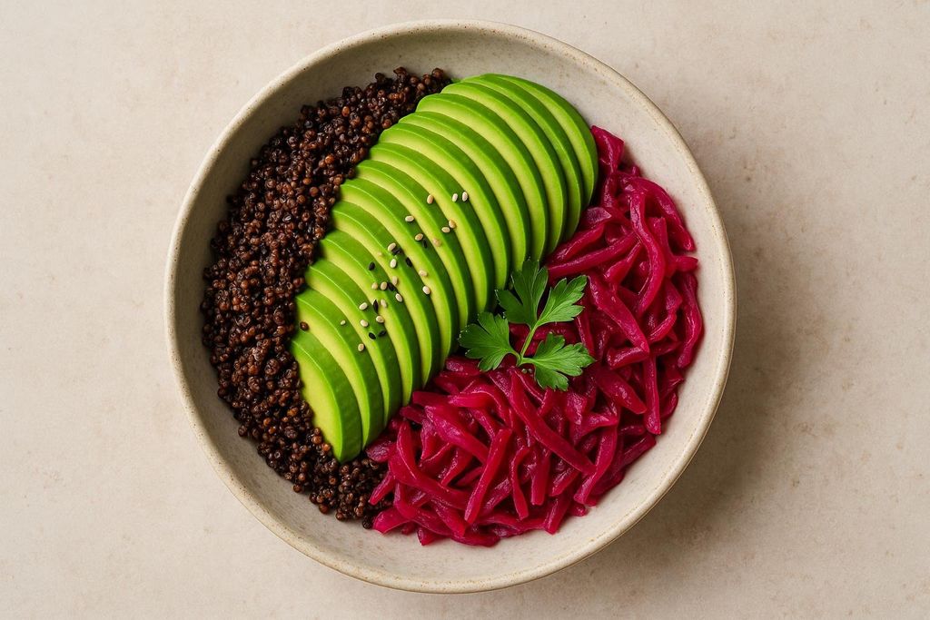 A close-up shot of a nutritious grain bowl containing black quinoa, thinly sliced avocado topped with sesame seeds, and bright pink pickled cabbage, garnished with a sprig of parsley.
