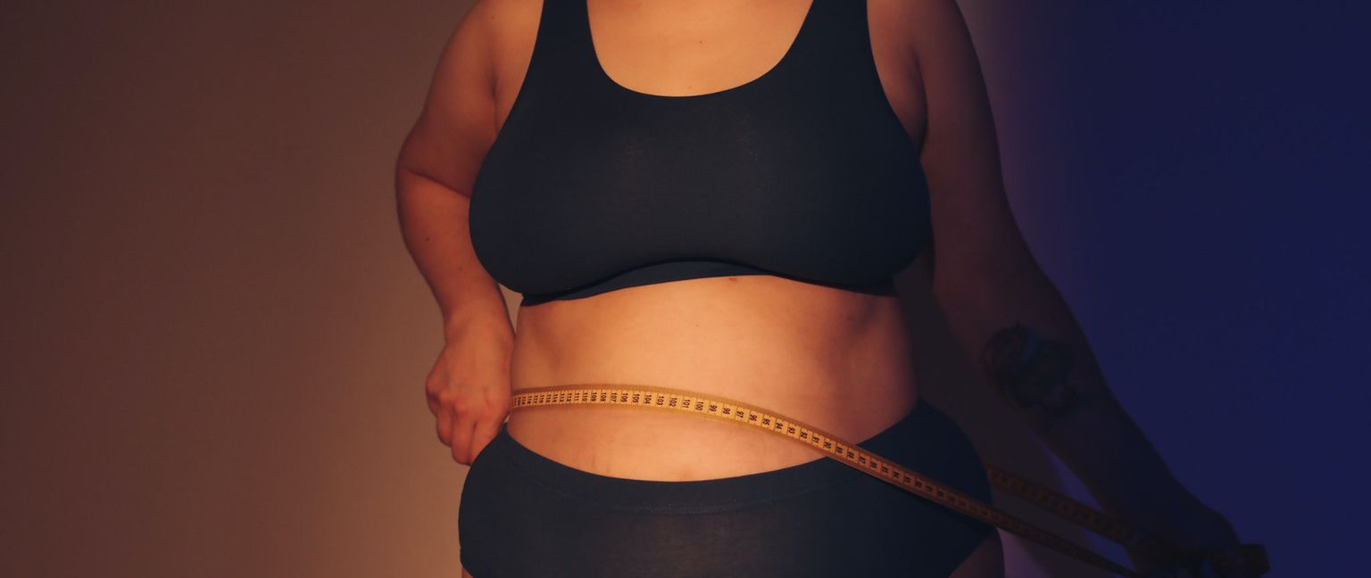A woman measuring her stomach with a yellow measuring tape.