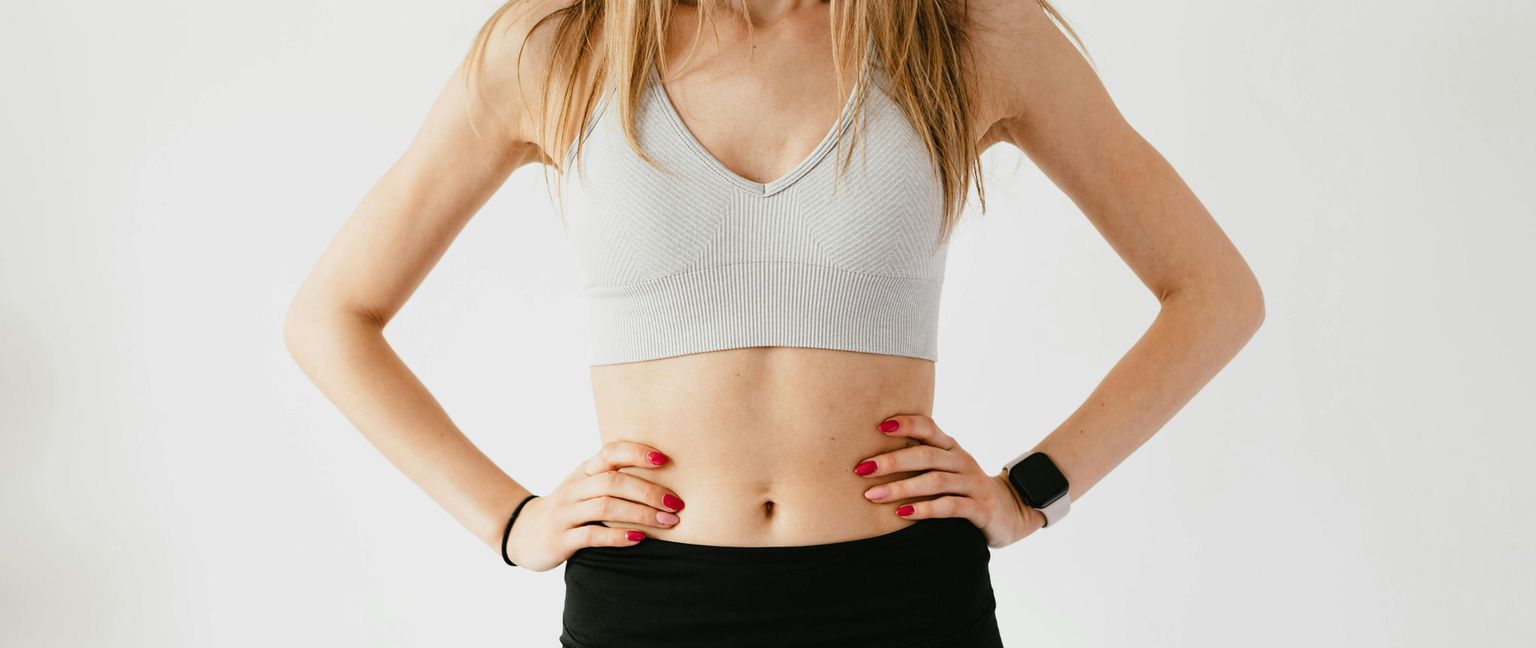 A woman with blonde hair in a gray sports bra and black leggings stands with her hands on her waist.
