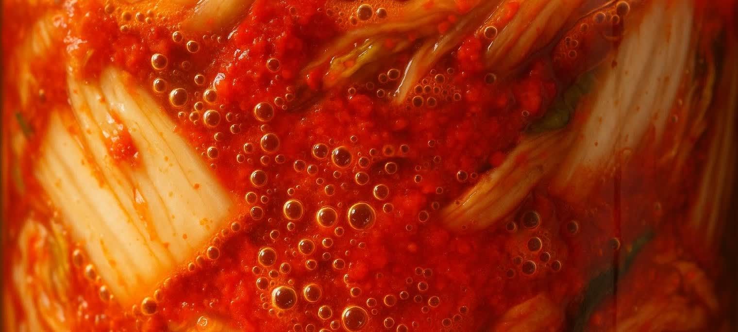 Close-up of numerous small bubbles on the surface of vibrant red kimchi, indicating fermentation.