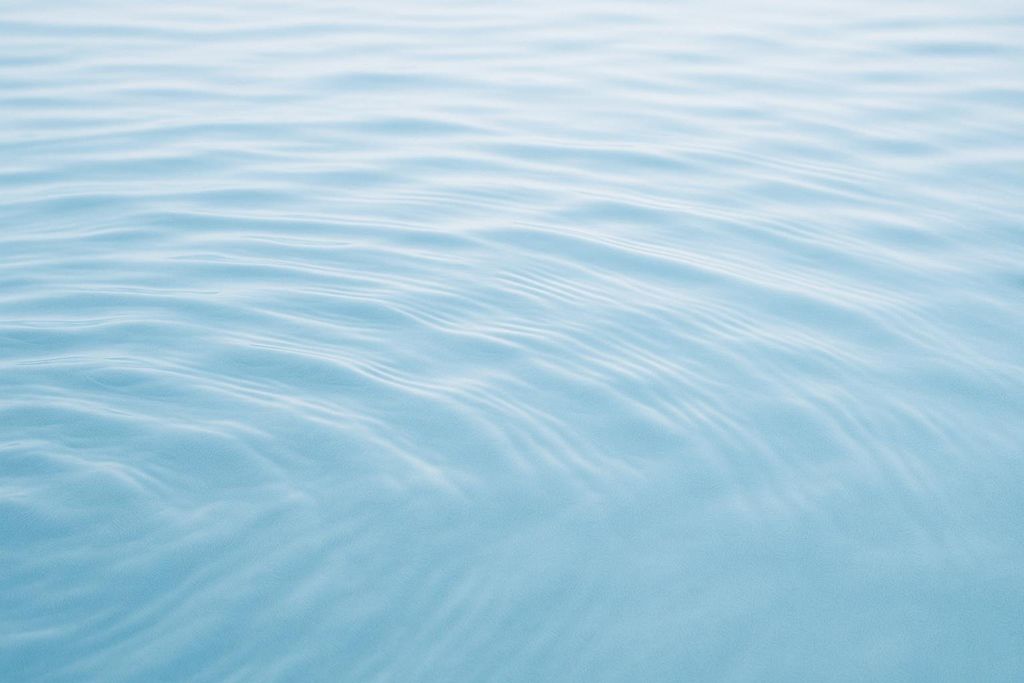 A close-up, abstract view of light blue water with gentle, undulating ripples across its surface.