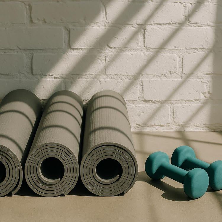 Rolled Pilates mats and small dumbbells resting against a sunlit wall