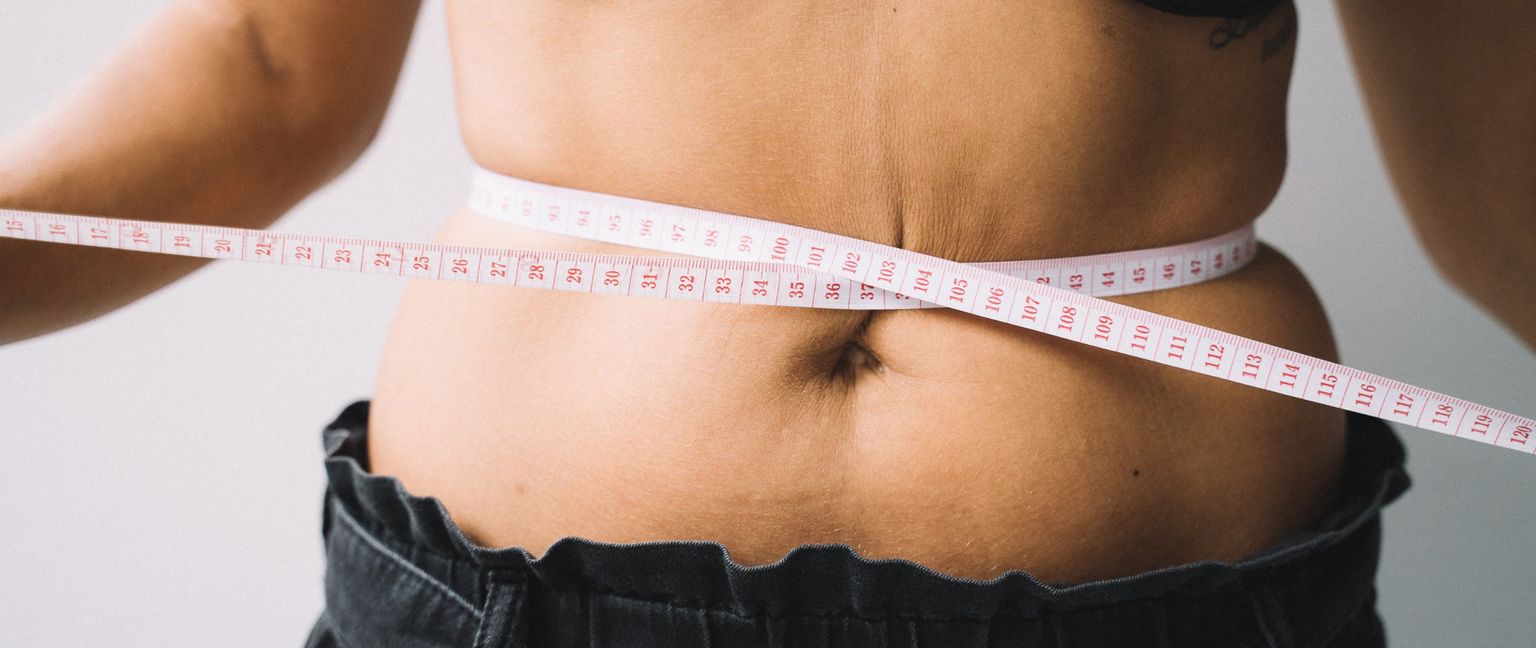 A person's midsection being measured with a white measuring tape around their waist.