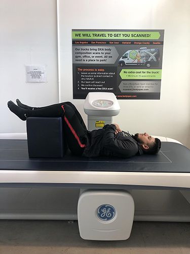 A person lying on a DXA scanner table with a pillow under their knees, preparing for a spine scan.
