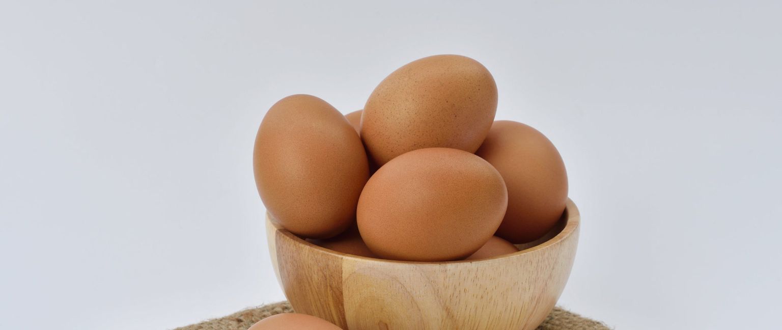Close up of brown eggs in a wooden bowl against a white background.