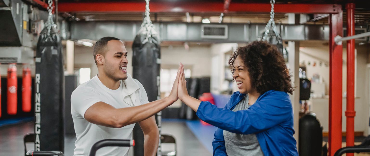 Two people at a gym high five each other, smiling.