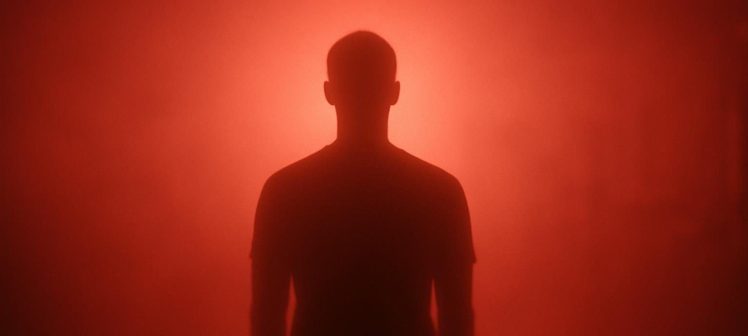 Silhouette of a person standing in a room illuminated by red light.