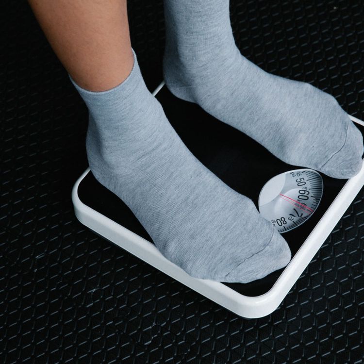 Feet in gray socks stand on a weight scale with the needle pointing towards 60 kg.