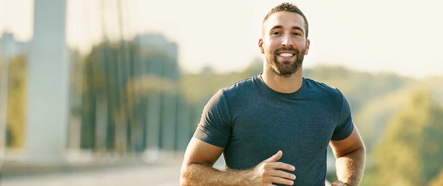 A man with a beard smiling while running outdoors.