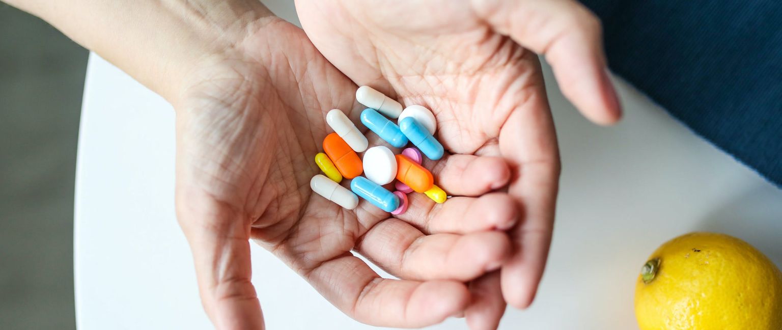 A pair of hands cupped together holding a pile of multi-colored pills and capsules.