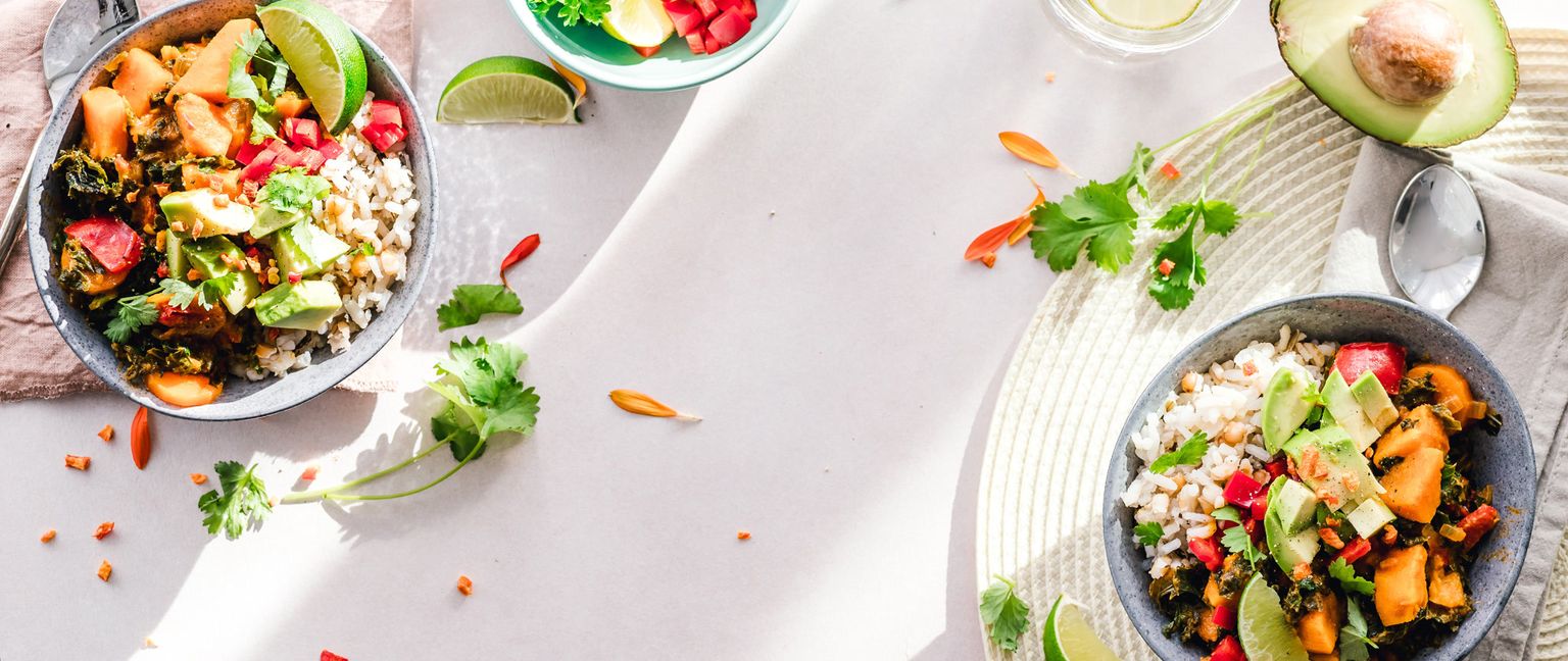 Two bowls of healthy rice bowls, each with rice, sweet potato, kale, avocado, tomatoes, and cilantro.