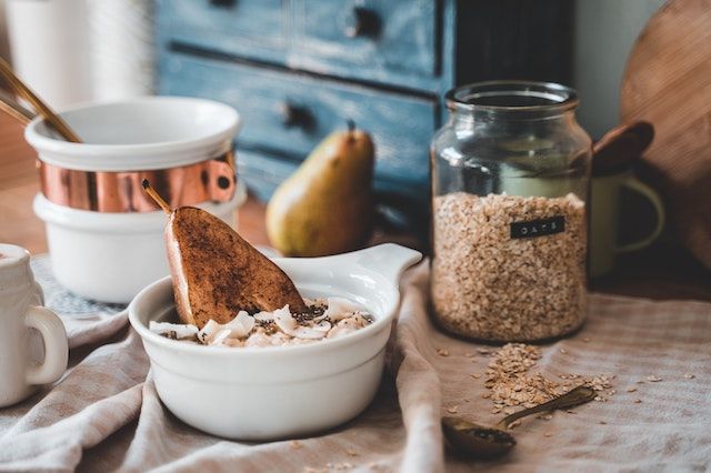 A bowl of oatmeal topped with sliced almonds, chia seeds, and a baked pear half.