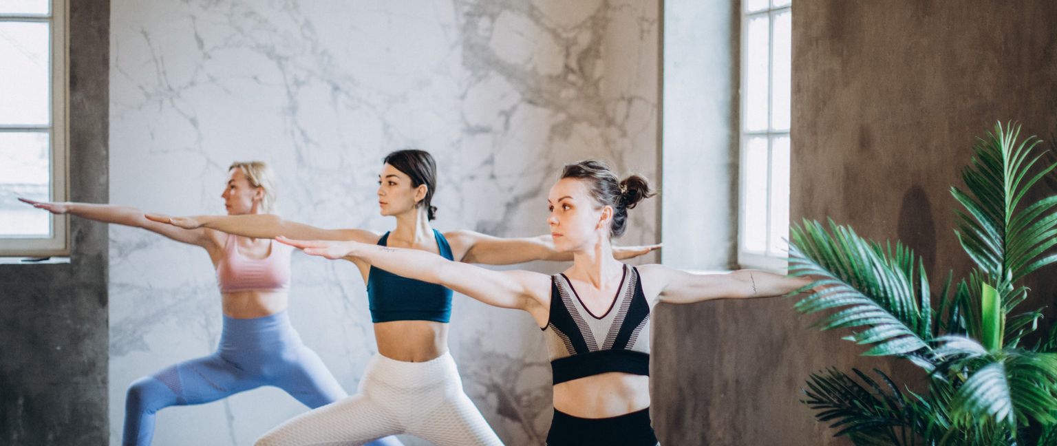 Three women in a yoga class in warrior pose.
