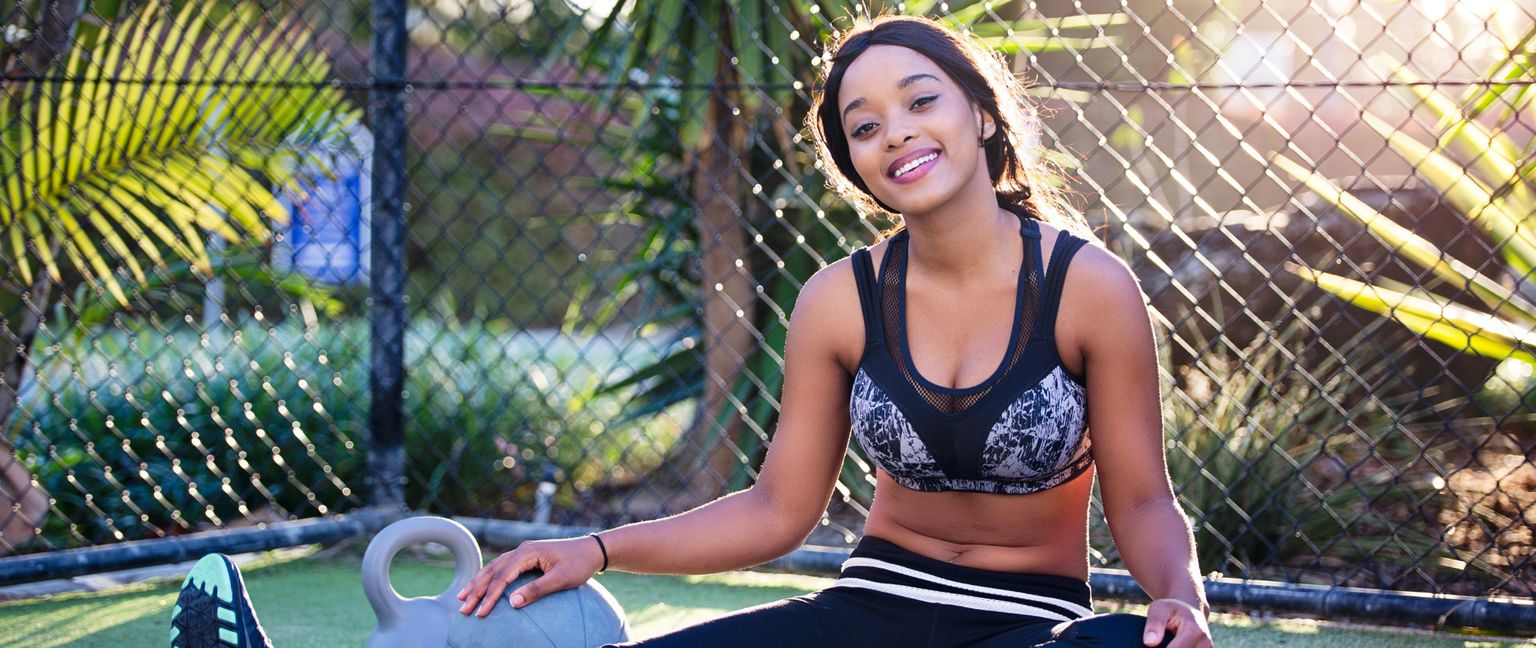A woman sits with a hand resting on a kettlebell, smiling at the camera.