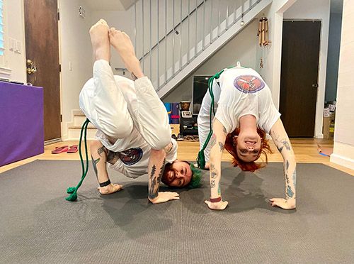 Two skilled individuals in white capoeira uniforms executing advanced poses on a workout mat.