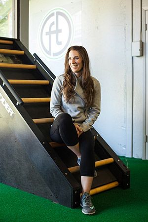 A woman in athletic wear sitting on a climbing ladder at a gym, looking to the side and smiling.