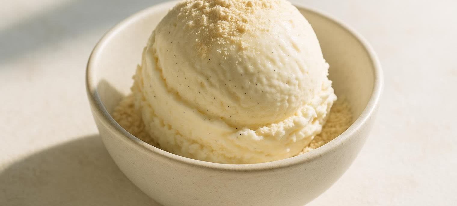 A perfect scoop of creamy vanilla protein ice cream in a light-colored bowl, sprinkled with a fine powder.