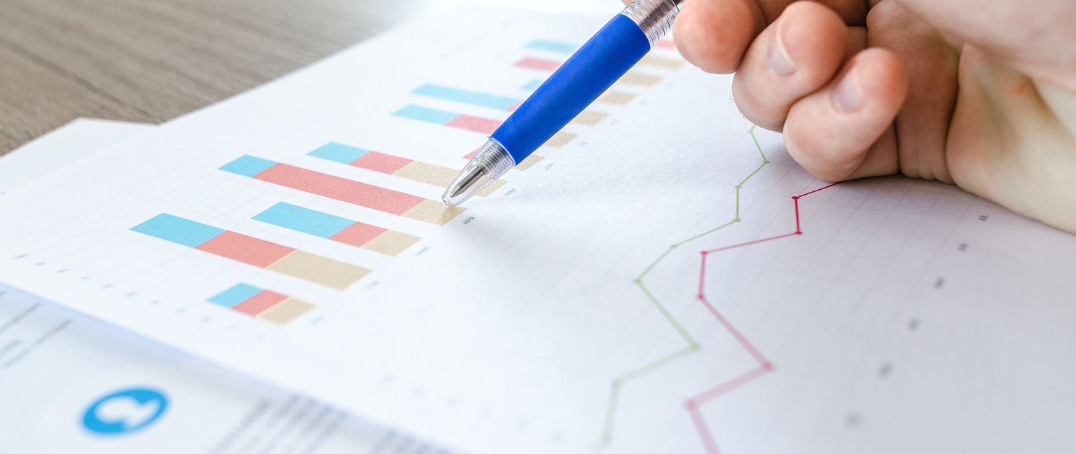 A hand holding a blue pen points to a stacked bar chart on a data report.