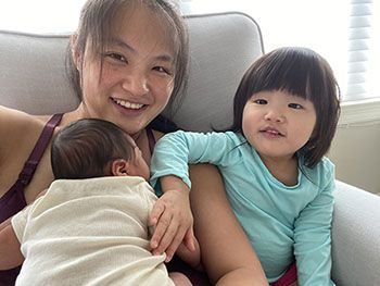 A mother holding a newborn baby, with a toddler sitting beside them.
