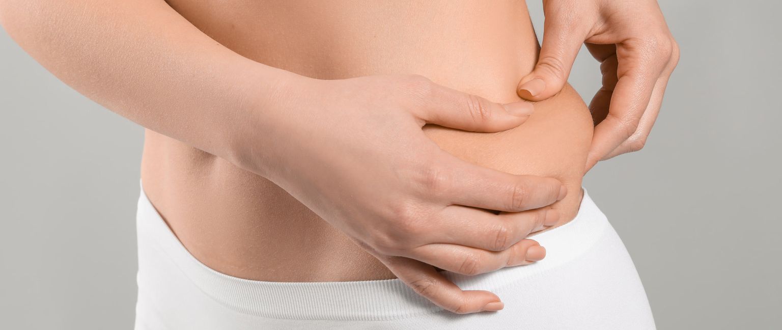 Close-up side view of a woman pinching the skin on her side with her fingers.