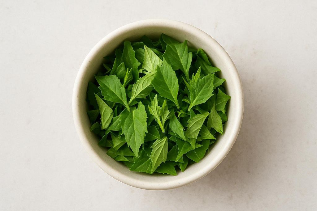 A top-down view of a bowl filled with chopped green leaves, representing a suggested serving size of Gynura procumbens.