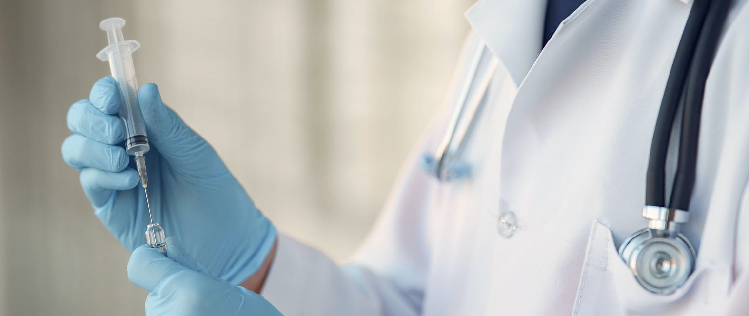 A close-up of a doctor in blue gloves filling a syringe from a small vial.
