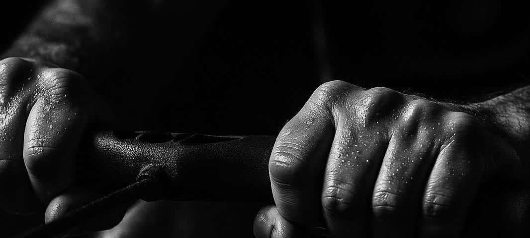 Close-up of sweaty hands tightly gripping the handle of a rowing machine, with droplets of sweat visible on the skin, set against a dark background emphasizing the intensity of a workout.