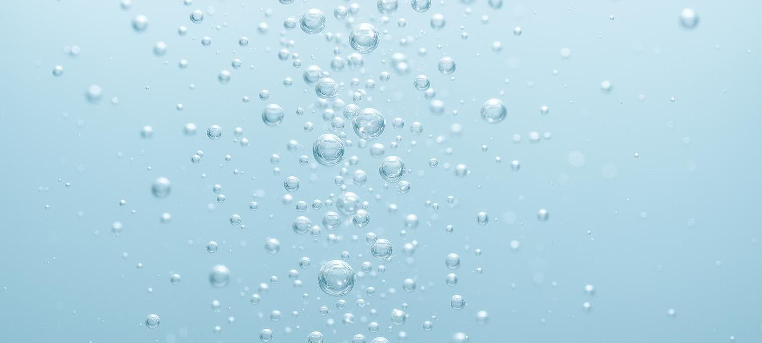 Close-up macro shot of tiny, shimmering bubbles ascending through clear water against a light blue background.
