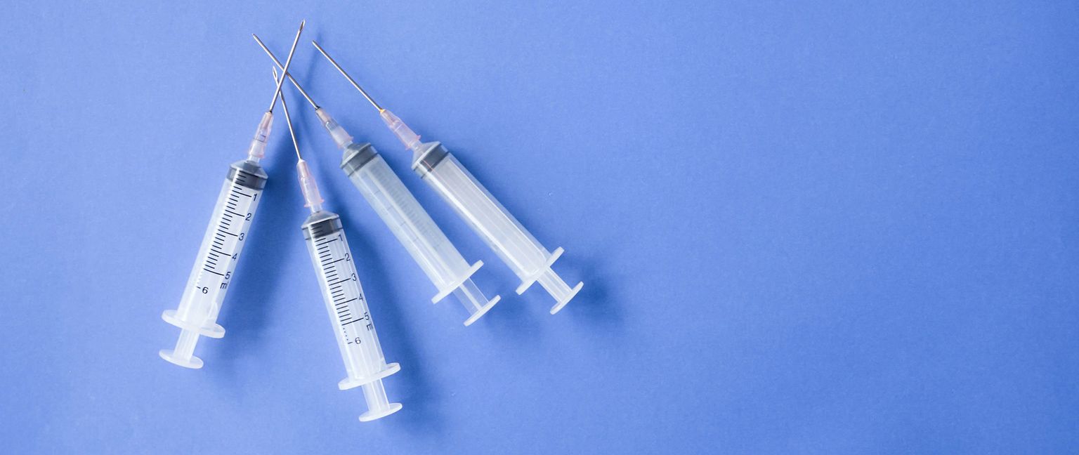 Several sterile syringes with needles lie on a blue surface.