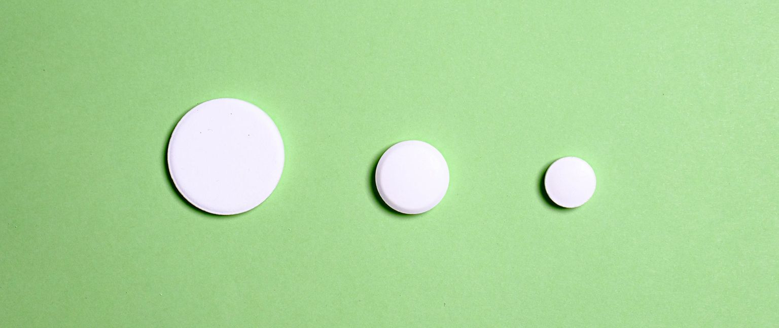 Three white round pills of different sizes laid out horizontally on a solid green background.