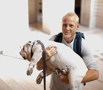 A man with a beard smiles and carries a large white dog in his arms.