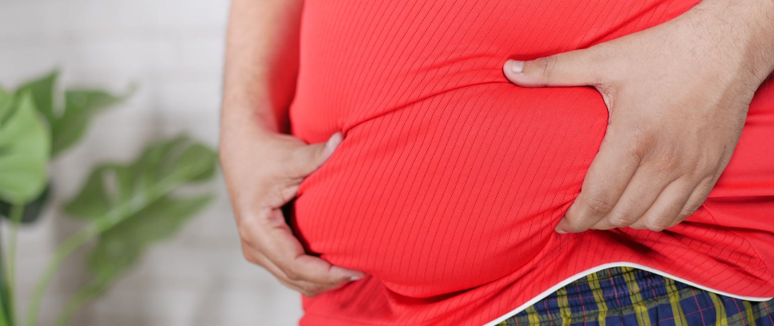 Close up of a person's midsection in a red shirt, holding onto their excess belly fat with both hands.