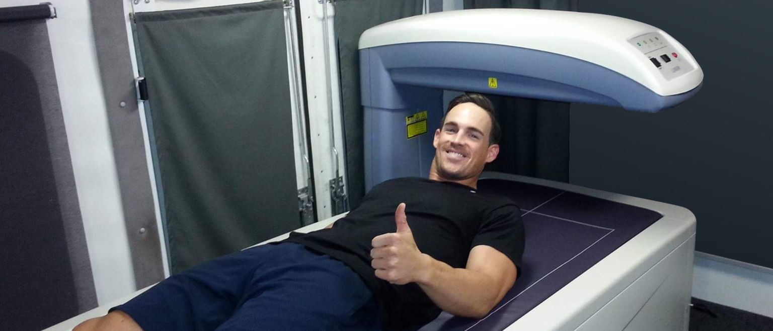 A man lying on a body scanner, smiling and giving a thumbs up.