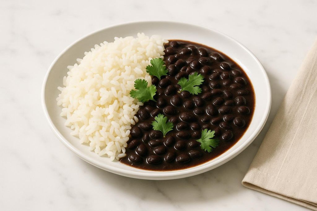A white plate holds a generous portion of white rice next to black beans in a dark sauce, garnished with several sprigs of green cilantro. A folded beige napkin is visible in the bottom right corner.