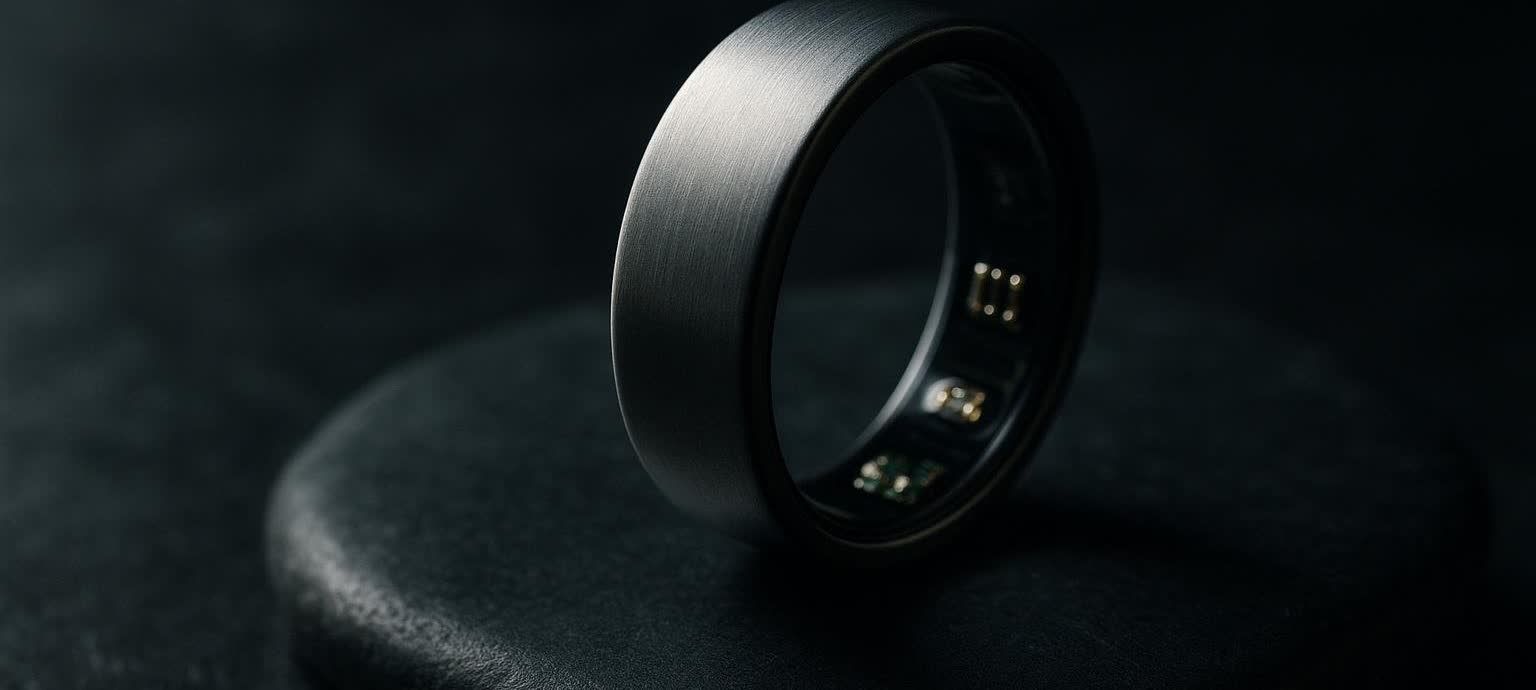 Close-up of a brushed titanium smart ring, showing its smooth exterior and gold-colored internal sensors against a dark, textured background.