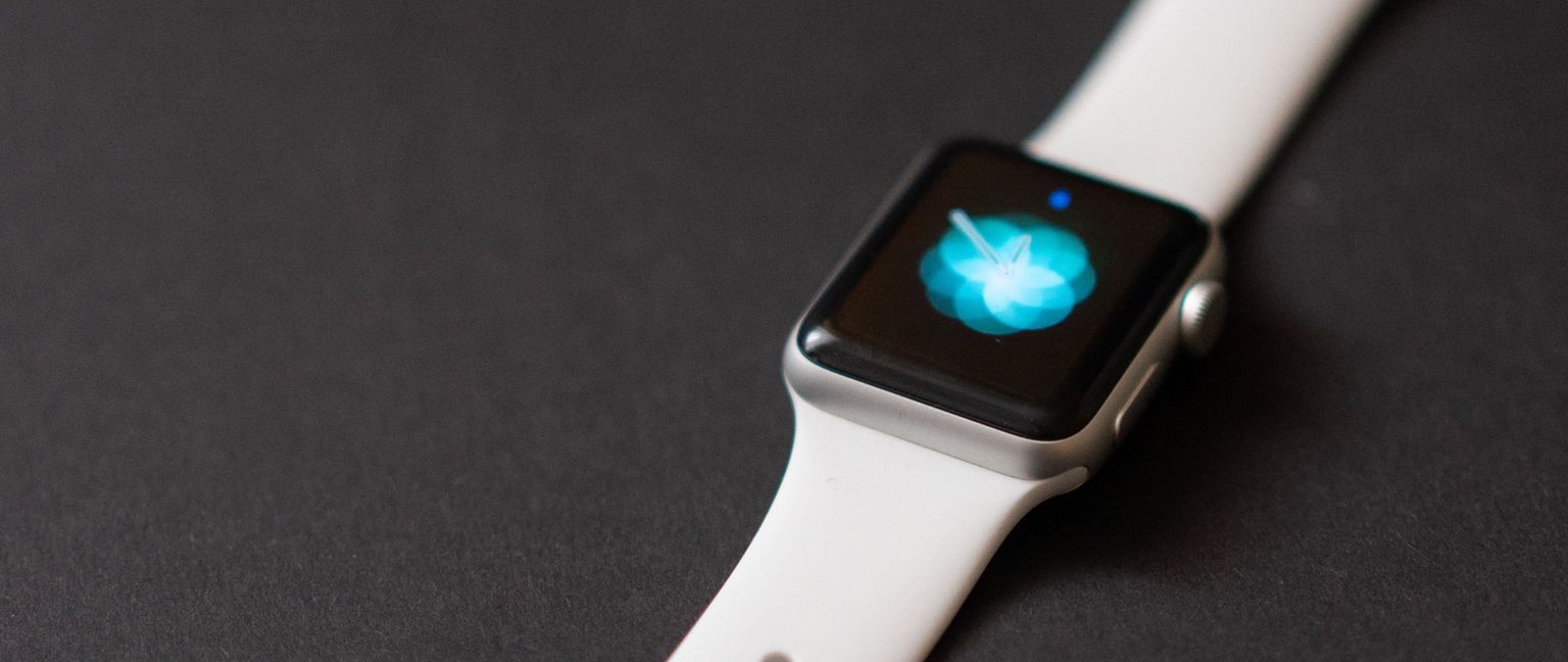 A close-up shot of a white Apple Watch with a blurred blue pattern on the screen.
