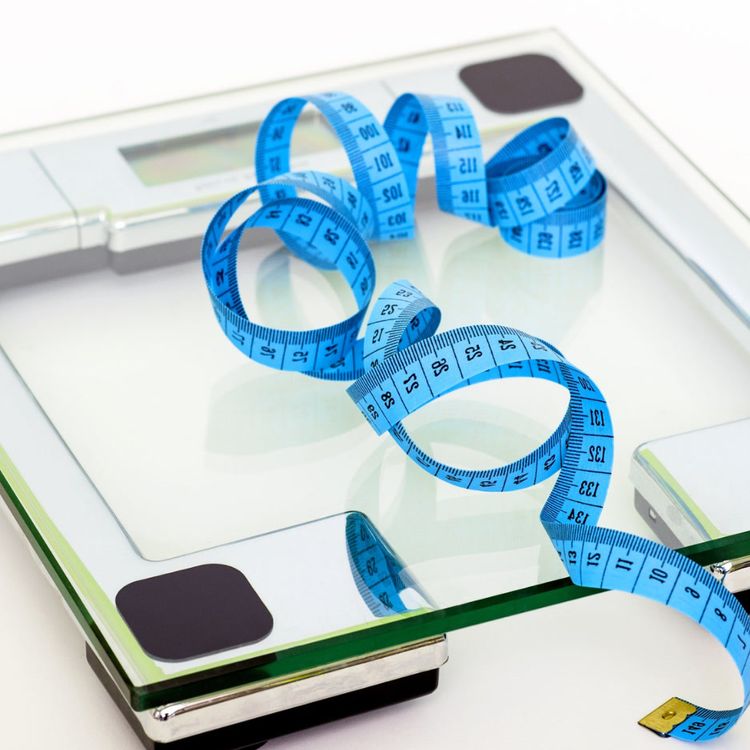 A weight scale with a blue tape measure resting on top of it.