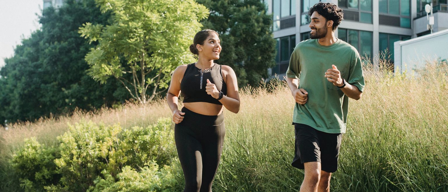A man and a woman are running and smiling together in a park on a sunny day.
