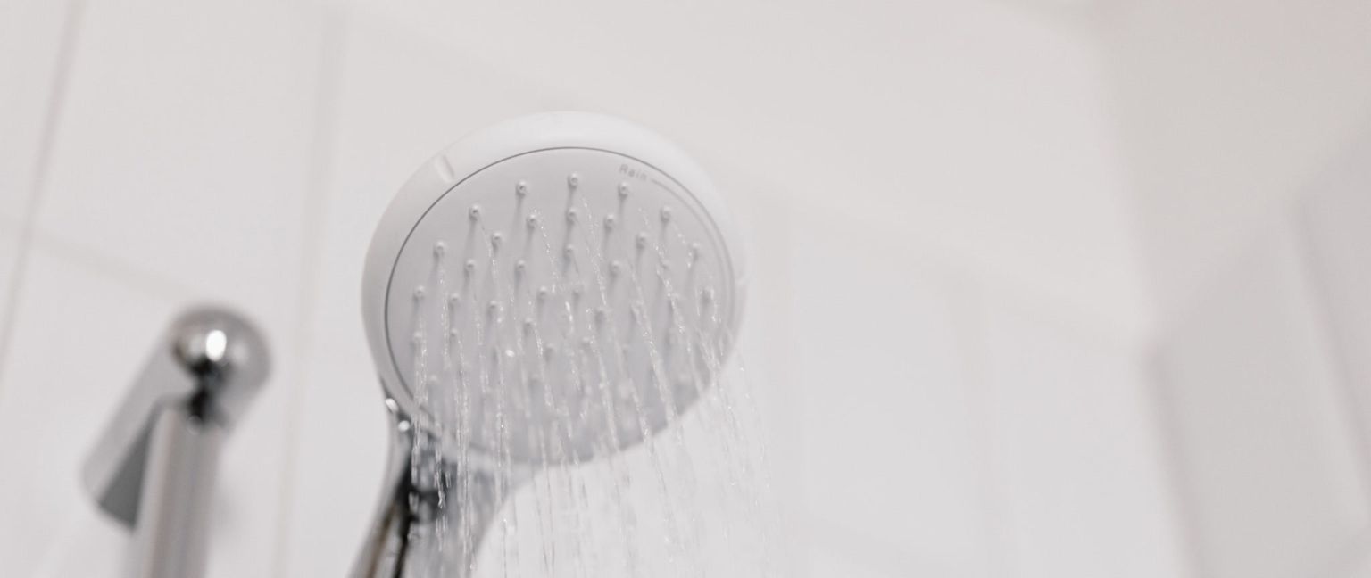 A close-up shot of a white shower head with water spraying out of it.